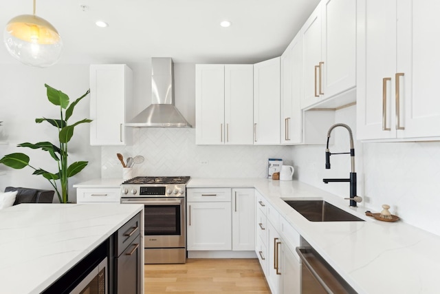 kitchen with stainless steel appliances, wall chimney exhaust hood, a sink, and white cabinets