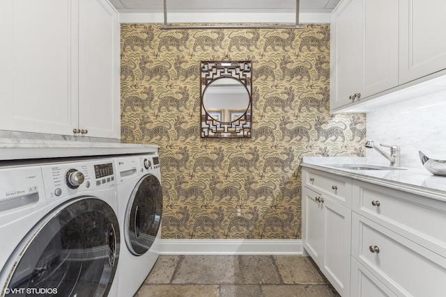 clothes washing area featuring cabinet space, wallpapered walls, stone tile flooring, separate washer and dryer, and a sink