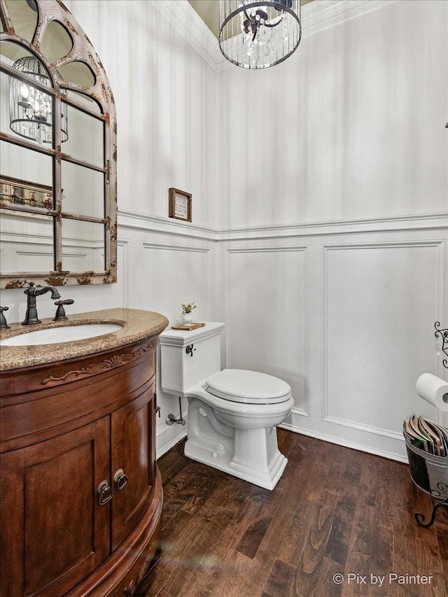 half bath with a decorative wall, vanity, toilet, and wood finished floors