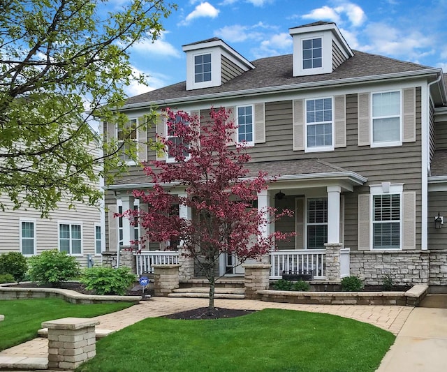 view of front of property with stone siding, a front yard, covered porch, and a shingled roof