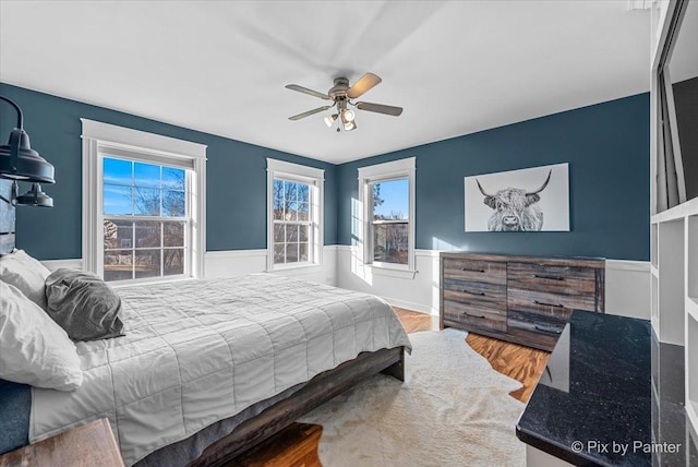 bedroom with a wainscoted wall, ceiling fan, and wood finished floors