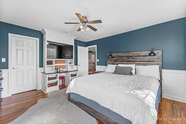 bedroom with a ceiling fan, wood finished floors, and wainscoting