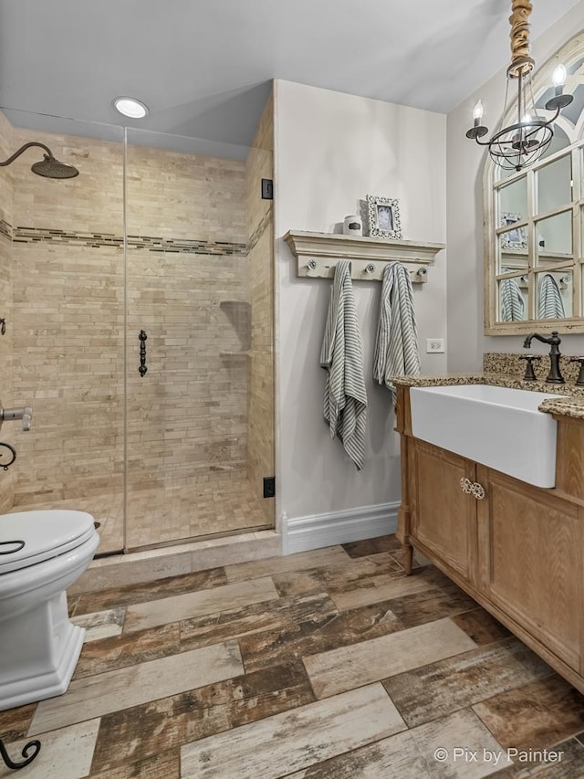 bathroom with baseboards, toilet, vanity, a shower stall, and a chandelier