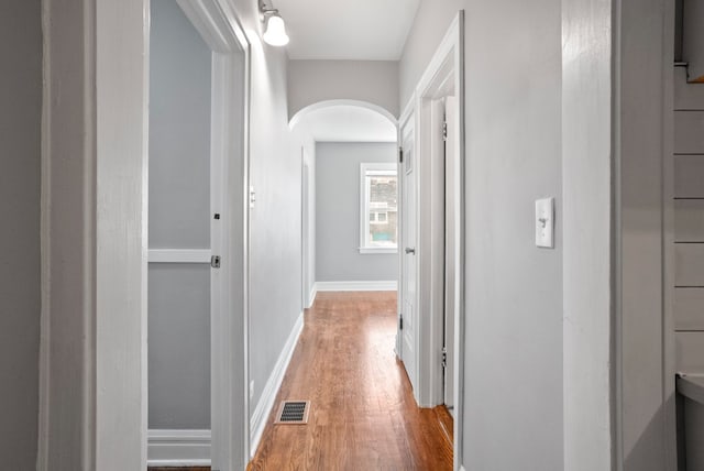 hall with arched walkways, light wood-type flooring, visible vents, and baseboards