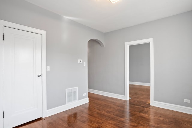 empty room with arched walkways, wood finished floors, visible vents, and baseboards