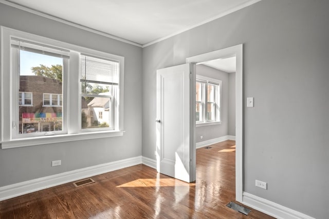 empty room featuring crown molding, wood finished floors, visible vents, and baseboards