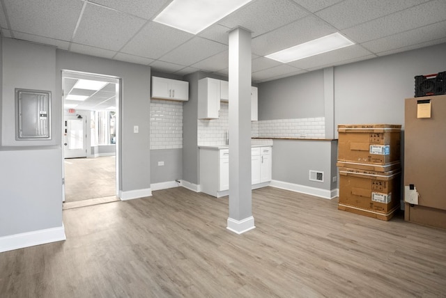 below grade area featuring visible vents, light wood-style flooring, a drop ceiling, electric panel, and baseboards