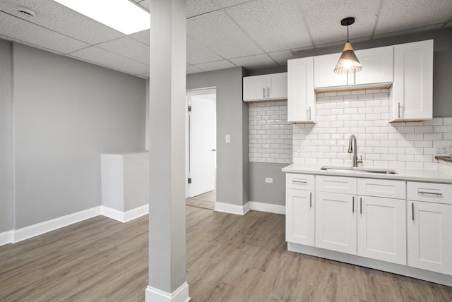 kitchen featuring light wood-style flooring, a sink, white cabinetry, light countertops, and decorative backsplash