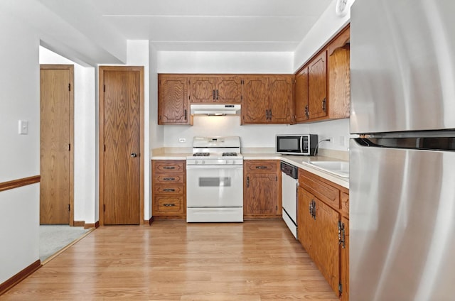 kitchen with appliances with stainless steel finishes, brown cabinets, light wood-style floors, and under cabinet range hood