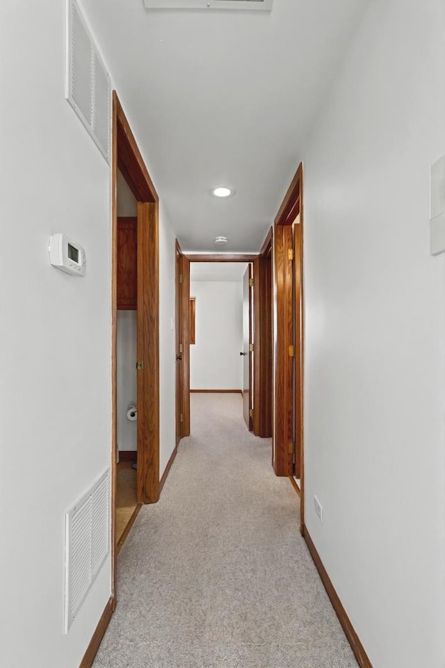 hall with baseboards, visible vents, and light colored carpet