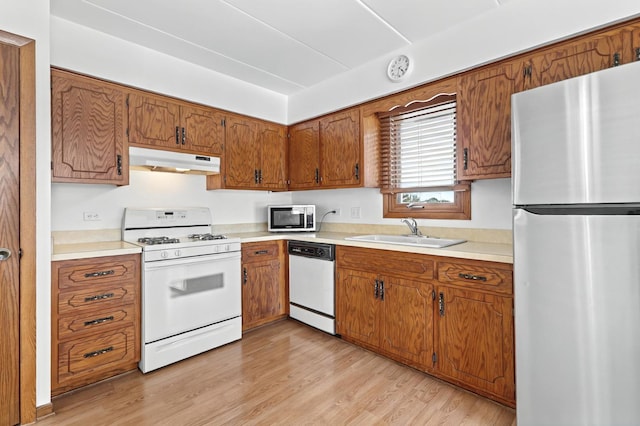 kitchen featuring light wood-style floors, brown cabinets, stainless steel appliances, under cabinet range hood, and a sink