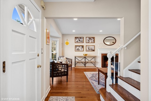 foyer entrance with a fireplace, recessed lighting, stairway, wood finished floors, and baseboards