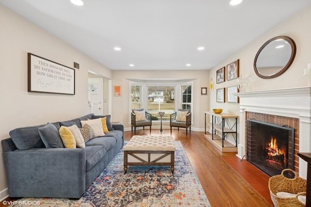 living area with recessed lighting, a brick fireplace, and wood finished floors