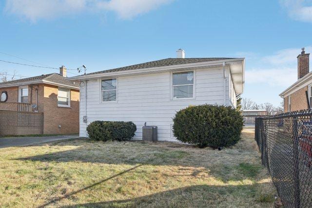 rear view of house featuring central air condition unit, a lawn, and fence