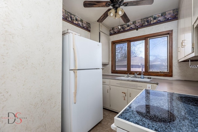 kitchen with ceiling fan, a textured wall, freestanding refrigerator, and white cabinetry