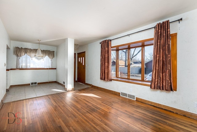 spare room with wood-type flooring, visible vents, and baseboards