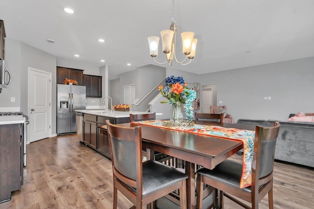 dining room featuring stairs, light wood-type flooring, a notable chandelier, and recessed lighting