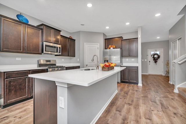 kitchen with appliances with stainless steel finishes, a sink, light wood-style flooring, and dark brown cabinetry