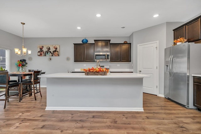 kitchen featuring stainless steel appliances, light countertops, a kitchen island with sink, dark brown cabinets, and wood finished floors