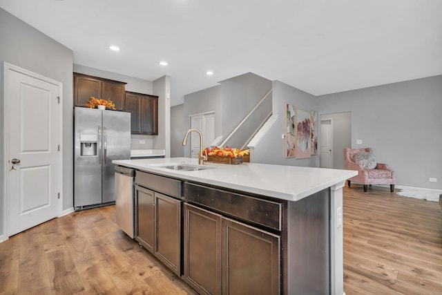 kitchen with a kitchen island with sink, a sink, light countertops, appliances with stainless steel finishes, and light wood finished floors