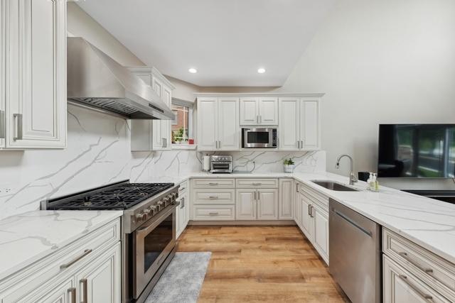 kitchen with tasteful backsplash, custom range hood, light stone counters, stainless steel appliances, and a sink