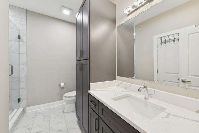 bathroom featuring toilet, vanity, baseboards, marble finish floor, and a stall shower