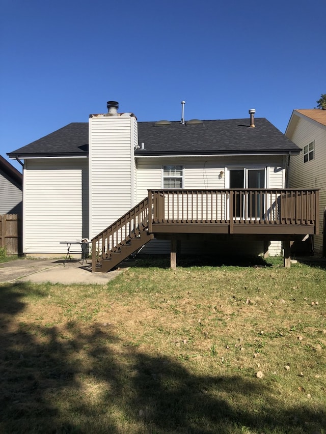 back of house with a chimney, roof with shingles, fence, a deck, and a yard