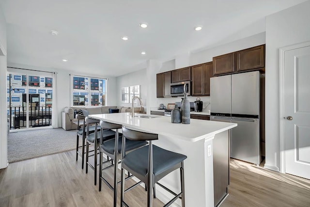 kitchen featuring a center island with sink, stainless steel appliances, a sink, dark brown cabinetry, and a kitchen bar