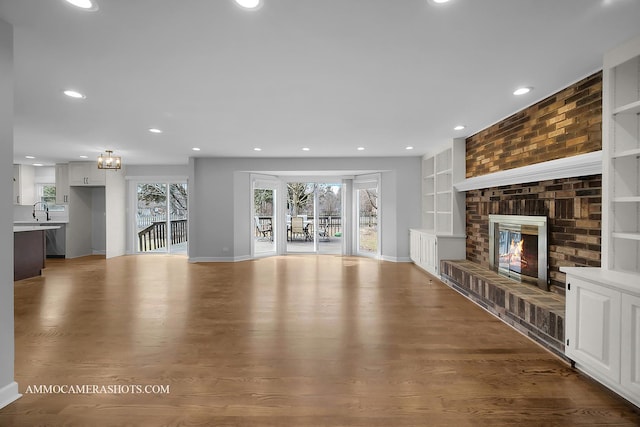 unfurnished living room with a fireplace, wood finished floors, a sink, and recessed lighting