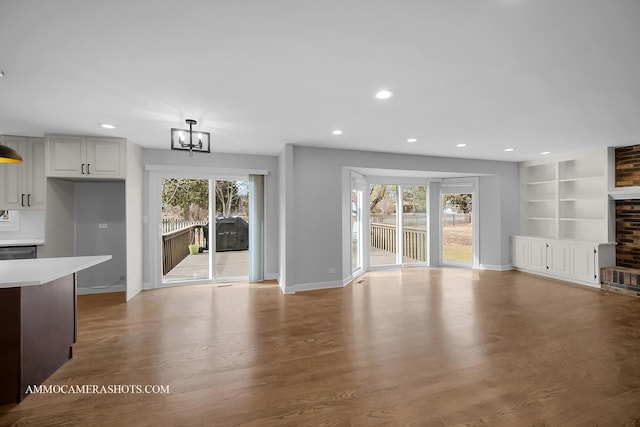 unfurnished living room with recessed lighting, a healthy amount of sunlight, baseboards, and wood finished floors