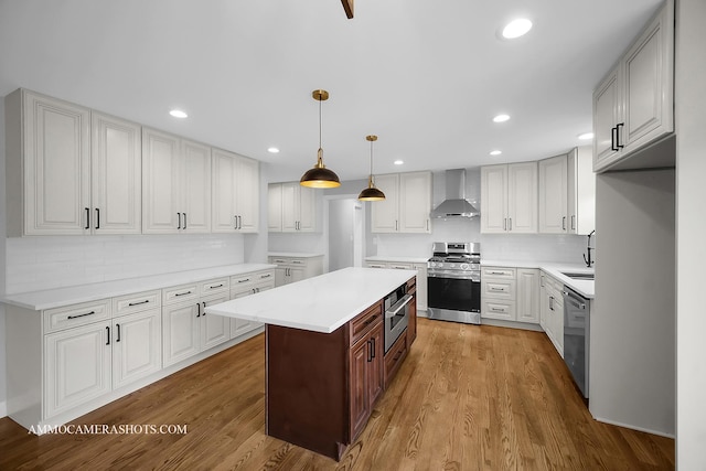 kitchen with stainless steel appliances, light countertops, a kitchen island, wood finished floors, and wall chimney exhaust hood