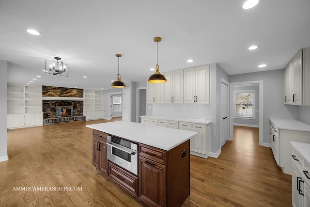 kitchen featuring wood finished floors, oven, light countertops, a brick fireplace, and recessed lighting