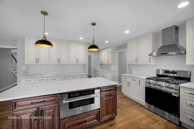 kitchen with light countertops, backsplash, appliances with stainless steel finishes, light wood-style floors, and wall chimney exhaust hood