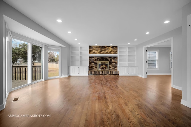 unfurnished living room with baseboards, visible vents, wood finished floors, a brick fireplace, and built in shelves