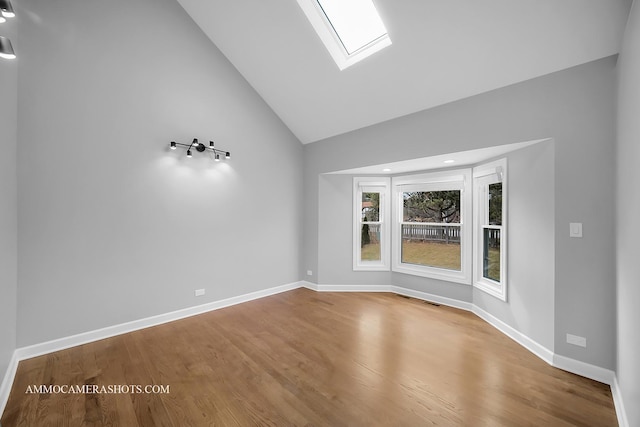 empty room with high vaulted ceiling, a skylight, wood finished floors, and baseboards