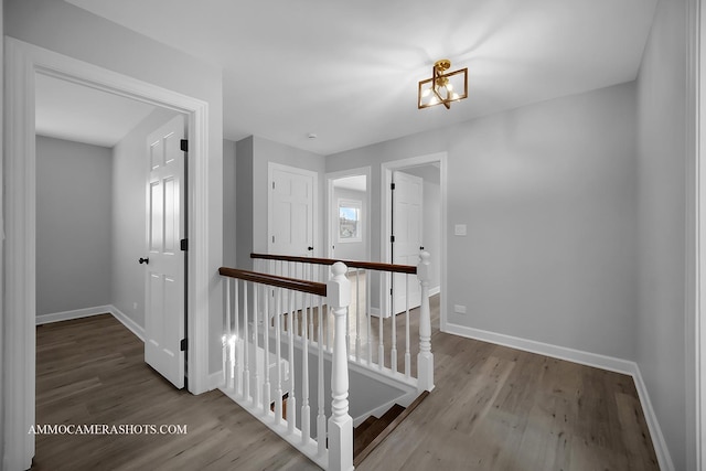 corridor with wood finished floors, an upstairs landing, and baseboards