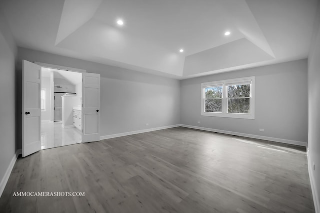 unfurnished bedroom featuring baseboards, a tray ceiling, and wood finished floors