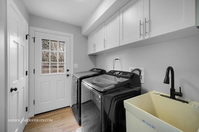 washroom featuring washing machine and dryer, cabinet space, a sink, and light wood finished floors