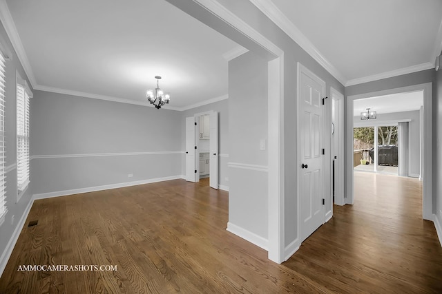 empty room with a chandelier, dark wood-style flooring, crown molding, and baseboards