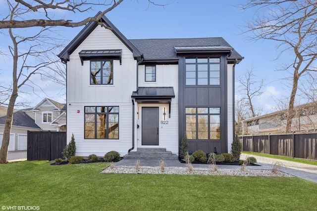 modern farmhouse style home with roof with shingles, a front lawn, board and batten siding, and fence