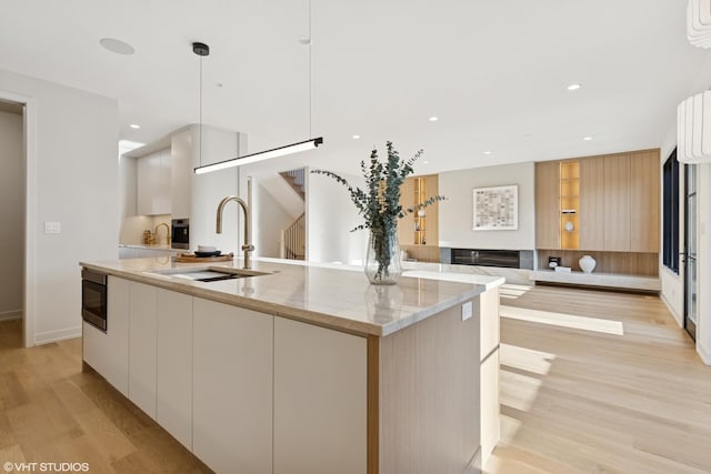 kitchen featuring modern cabinets, a sink, a center island with sink, and white cabinetry