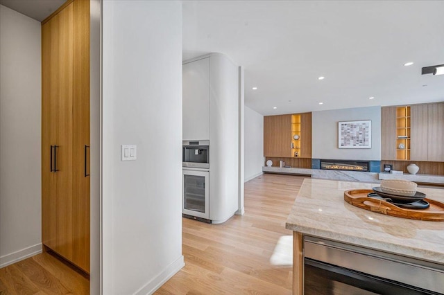 kitchen featuring light stone counters, oven, recessed lighting, light wood-type flooring, and a glass covered fireplace