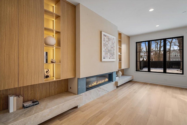 unfurnished living room featuring built in features, a glass covered fireplace, baseboards, and wood finished floors