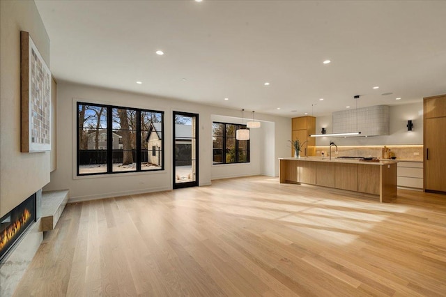 unfurnished living room with recessed lighting, a glass covered fireplace, a sink, light wood-type flooring, and baseboards