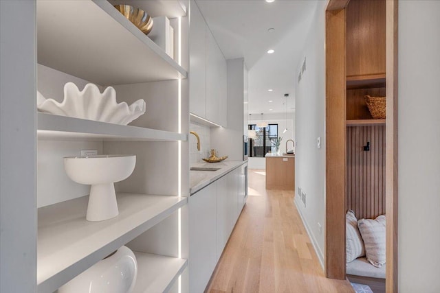 hall featuring light wood-type flooring, visible vents, a sink, and recessed lighting