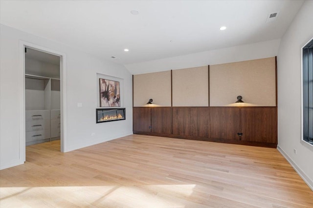 empty room featuring vaulted ceiling, light wood finished floors, a glass covered fireplace, and recessed lighting