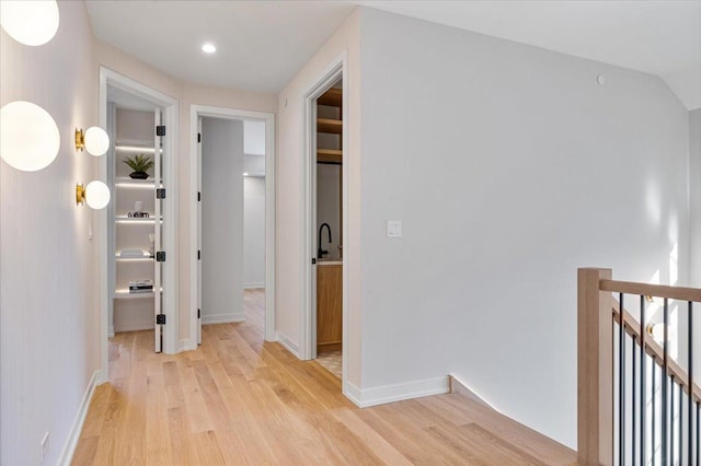 hall featuring light wood finished floors, recessed lighting, baseboards, and an upstairs landing