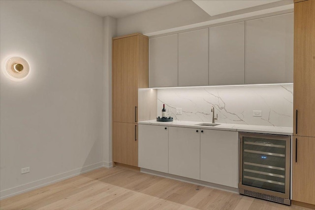 bar featuring light wood-style flooring, beverage cooler, a sink, baseboards, and tasteful backsplash