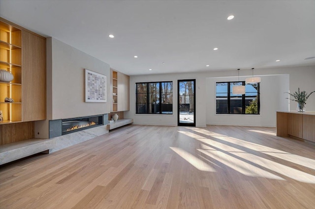 unfurnished living room with built in shelves, recessed lighting, light wood-style floors, a glass covered fireplace, and baseboards