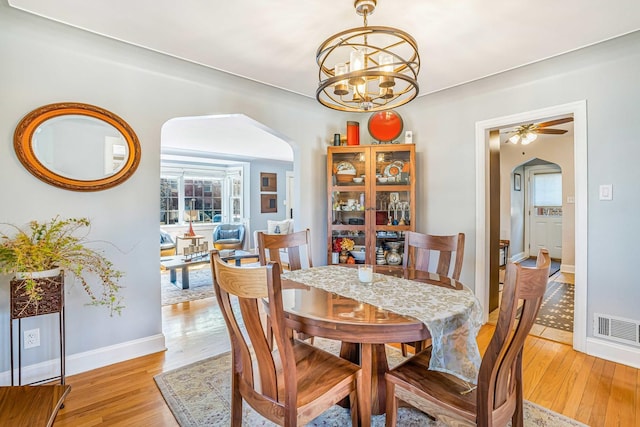 dining space with visible vents, arched walkways, and light wood-type flooring